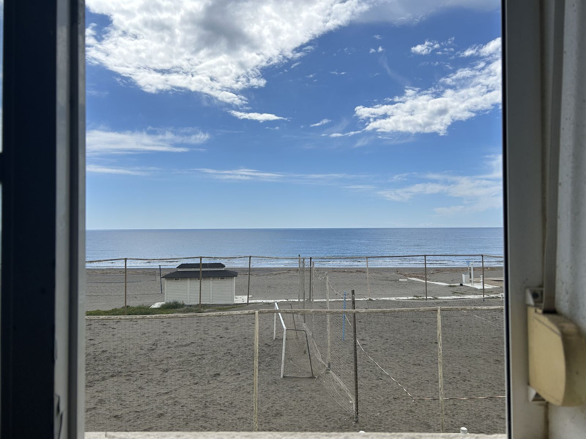 Strandzicht door het raam met zand, zee en blauwe lucht.