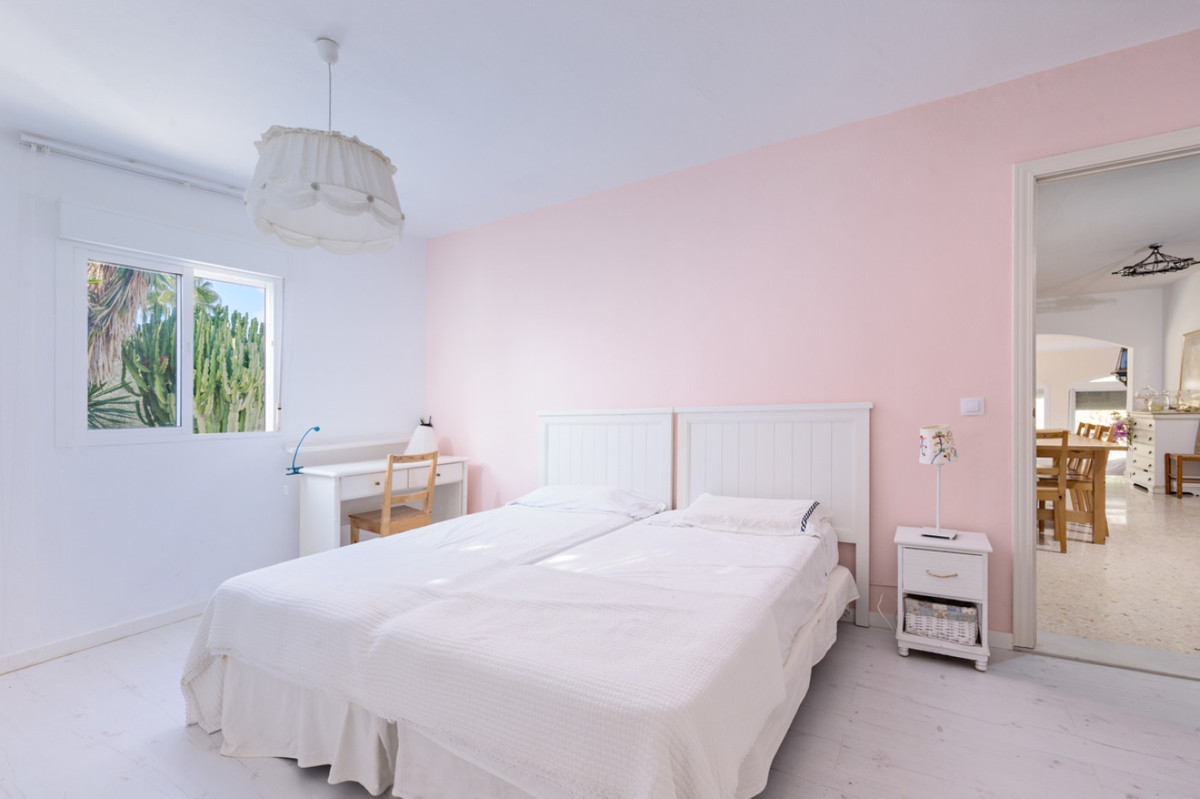 Lichte slaapkamer met roze muur en wit bed en bureau.