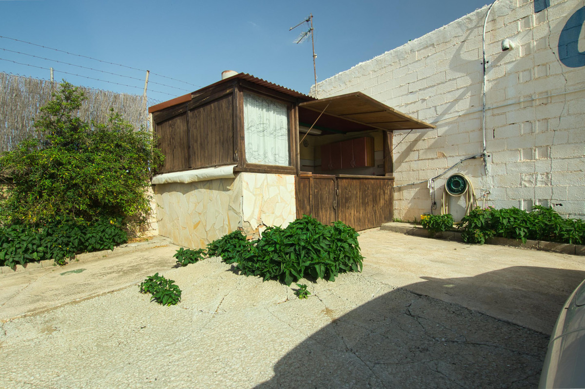 Kleine houten buitenkiosk met stenen fundering en begroeiing.