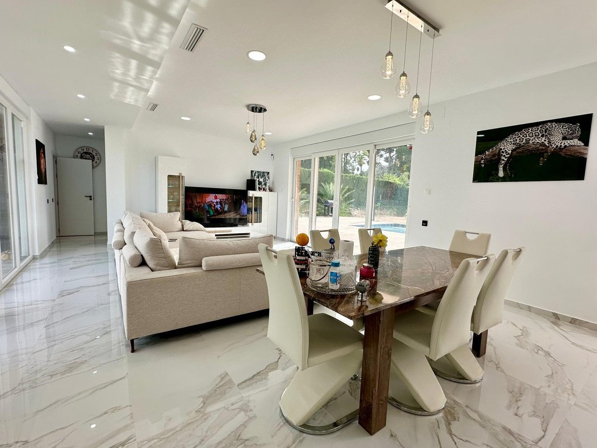 Spacious living and dining area with modern furniture, a large sofa, dining table, and garden view through glass doors.