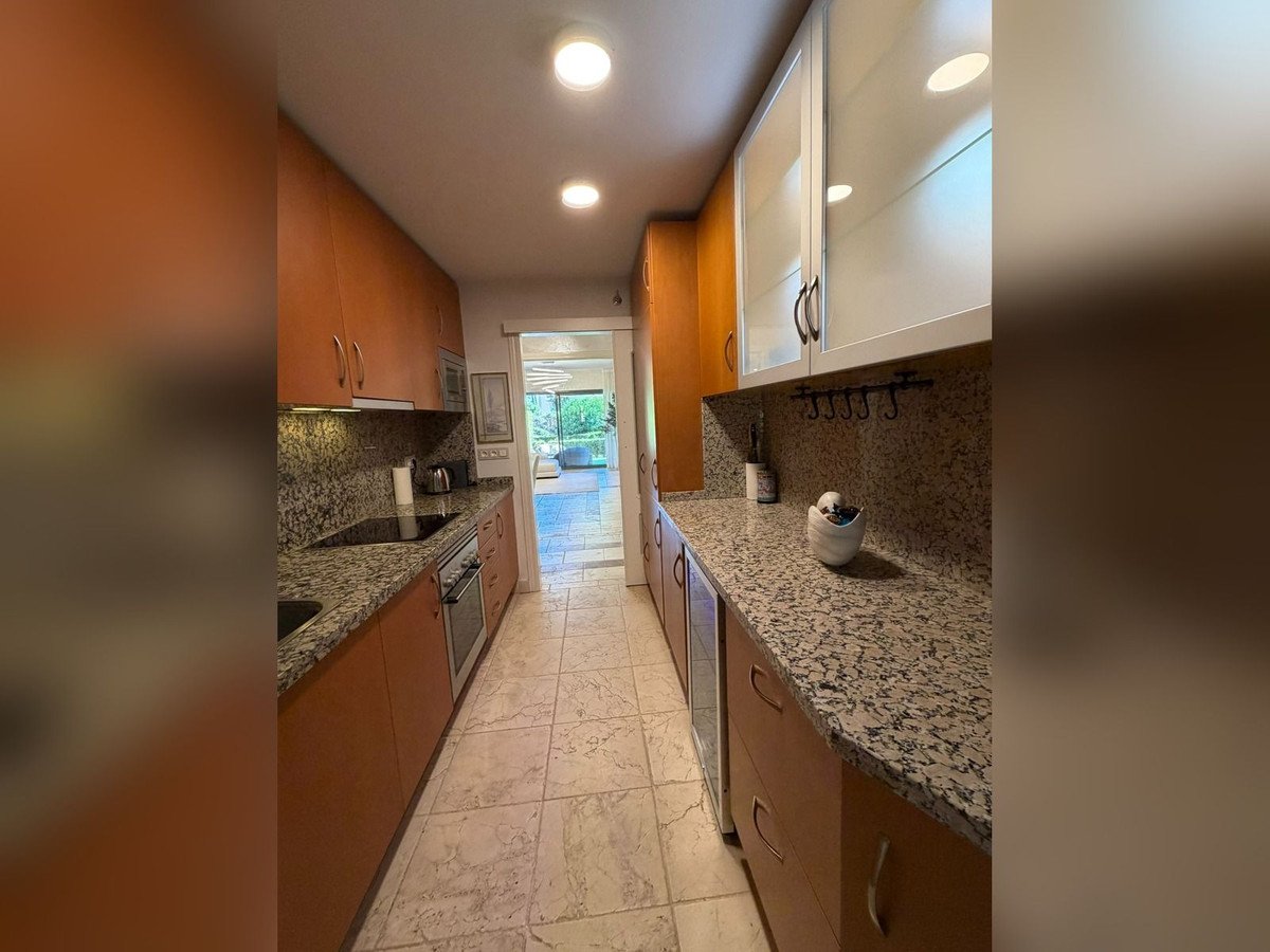 Long galley kitchen with granite countertops, cabinets, and a garden view through the doorway