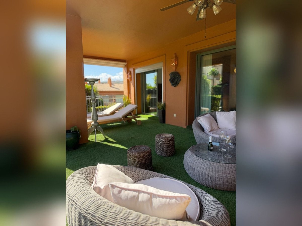 Outdoor lounge with wicker furniture, green artificial turf, and sunny views.