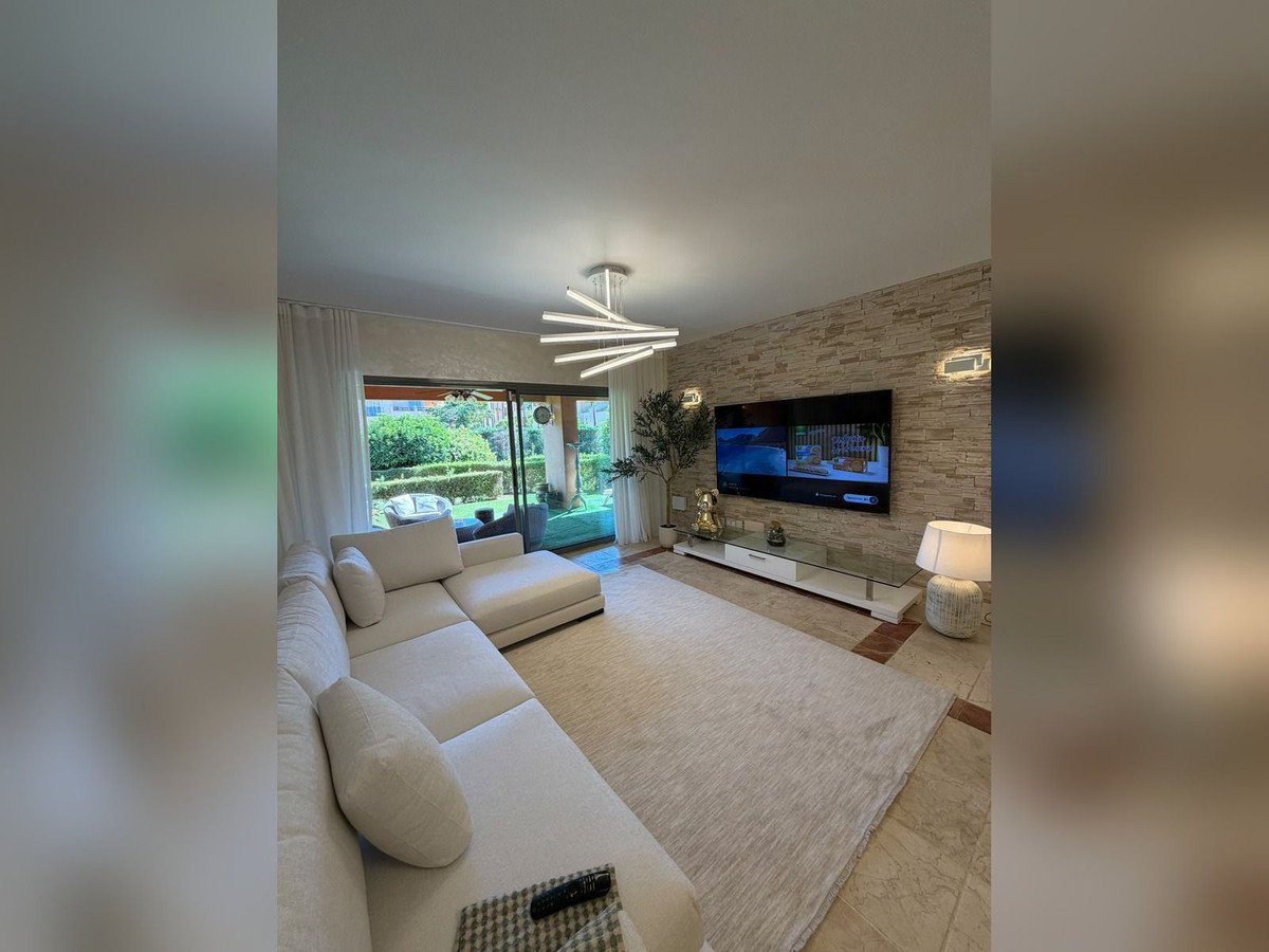 Modern living room with white sofa, stone wall, TV, and garden view through large windows