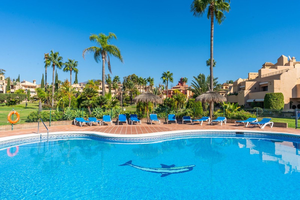 A resort swimming pool with lounge chairs and palm trees under a clear blue sky.