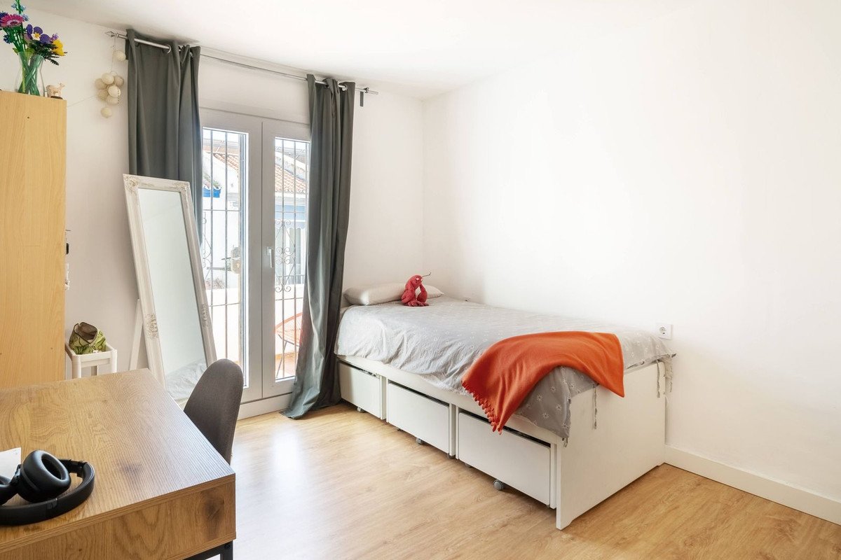 A bright bedroom with a single bed, desk, mirror, and glass door leading to a balcony.
