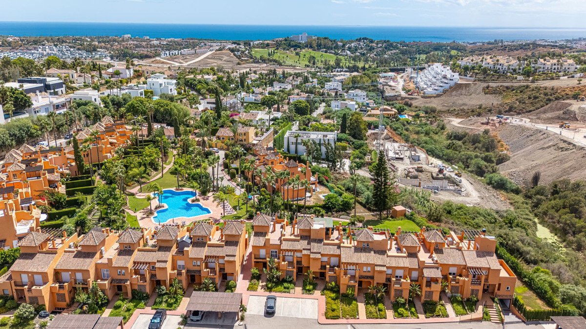 Aerial view of orange townhouses with a blue swimming pool and a distant view of the sea under a clear sky.