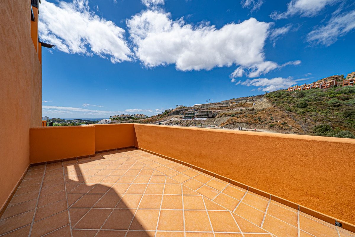 Terrace with orange walls and tiled floor, offering a view of the sea and hills with houses.