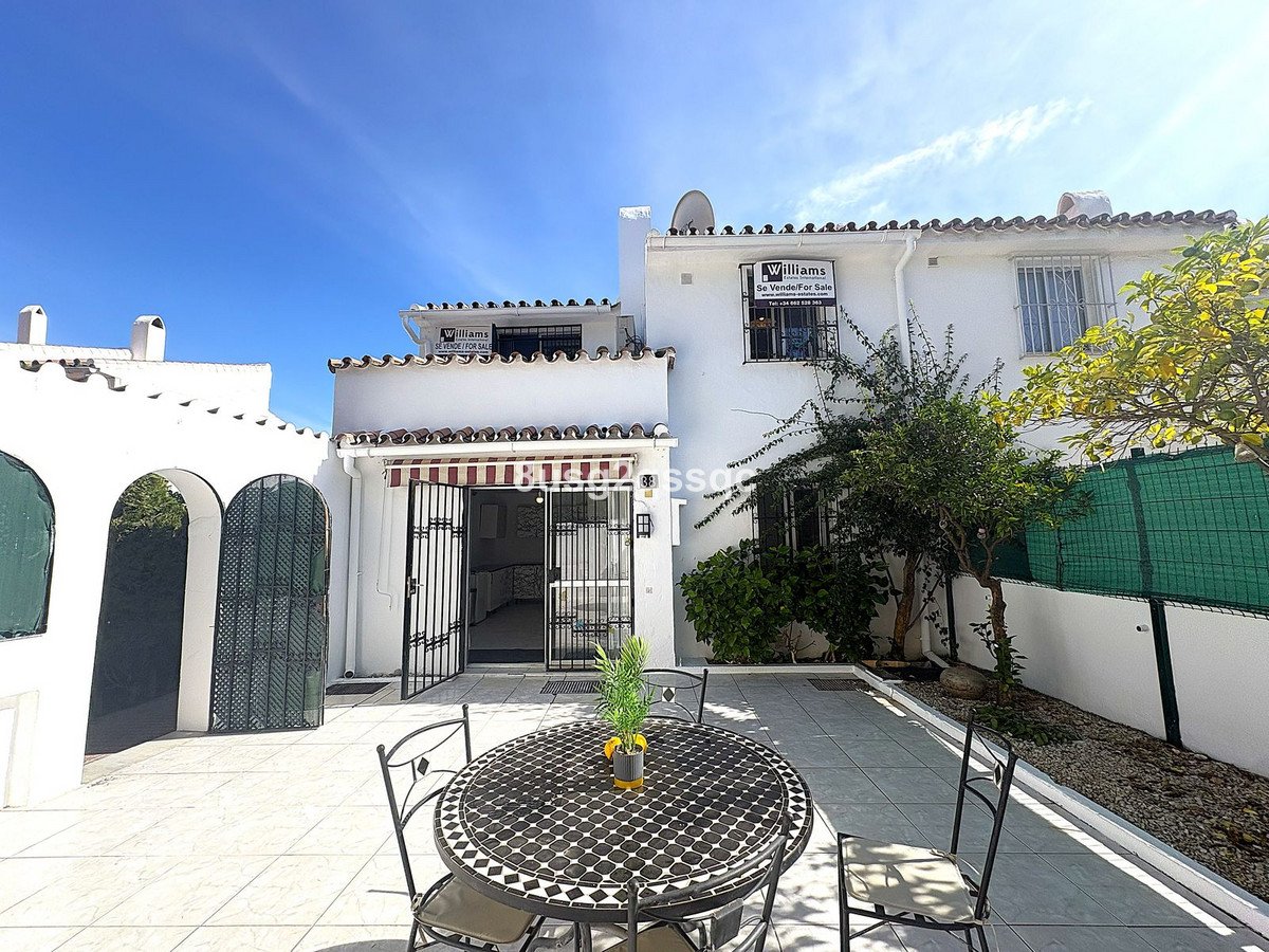 White villa with tiled patio, outdoor dining table, and garden view