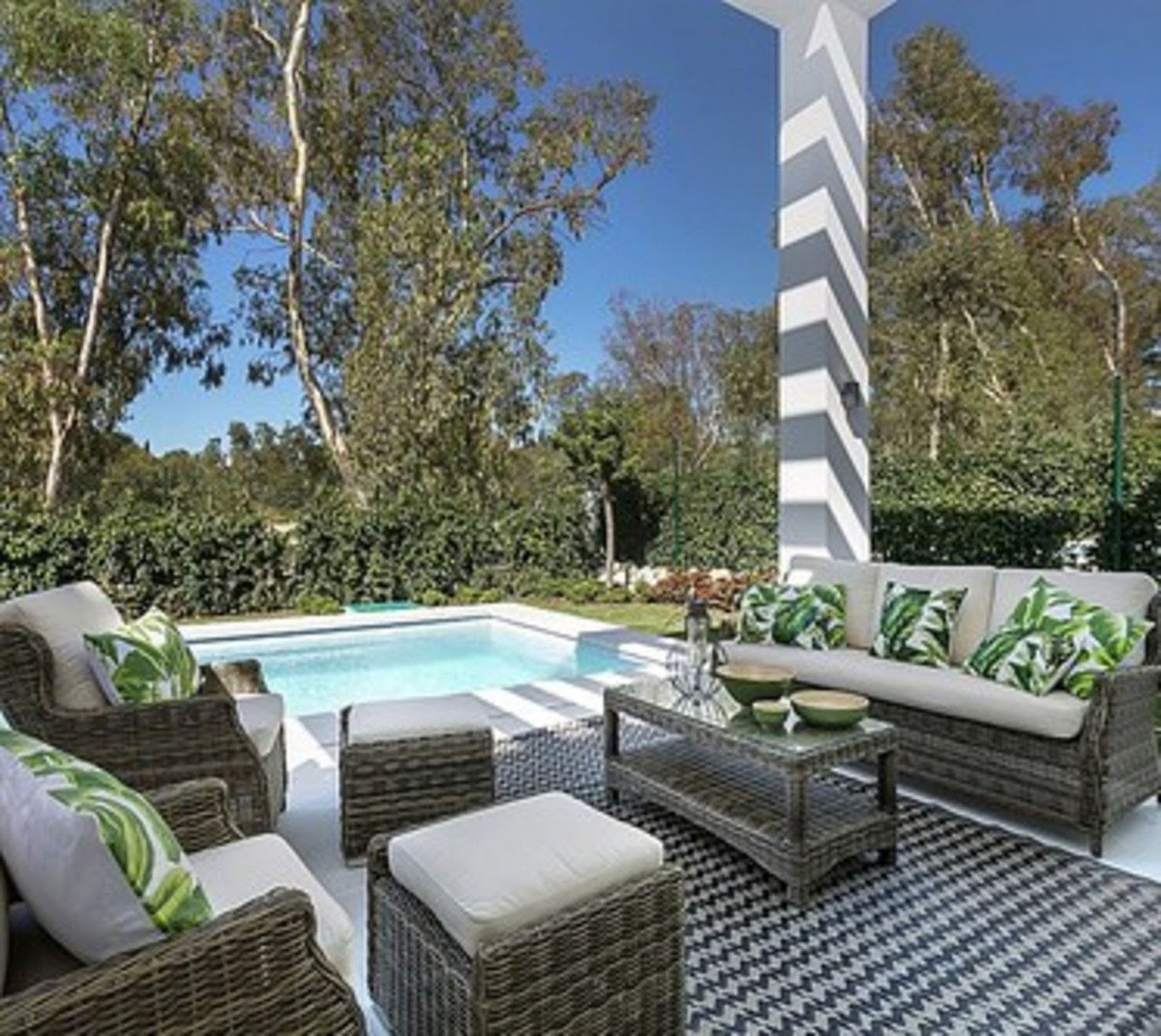 Outdoor patio with wicker furniture, coffee table, and a swimming pool, surrounded by greenery.