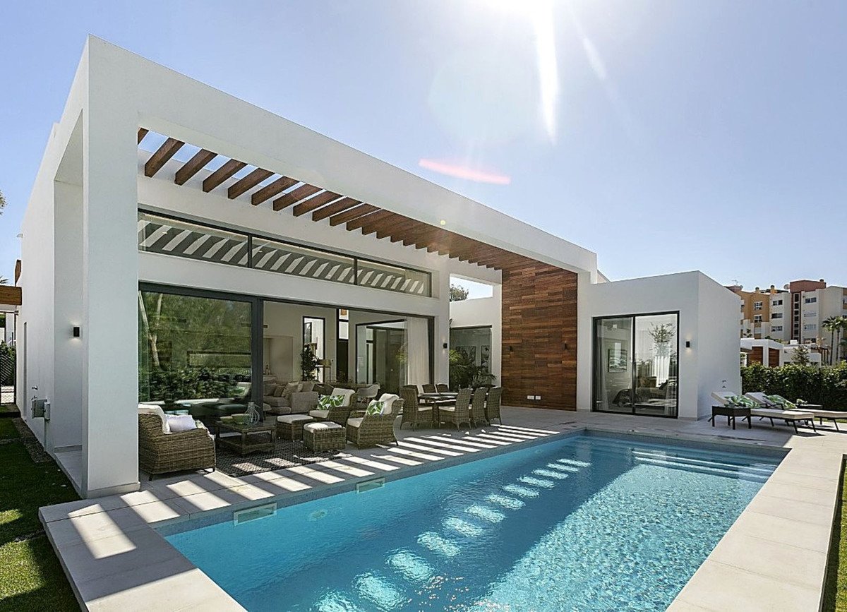 Modern villa exterior with swimming pool, outdoor lounge, and dining area, featuring large glass doors and wooden accents.