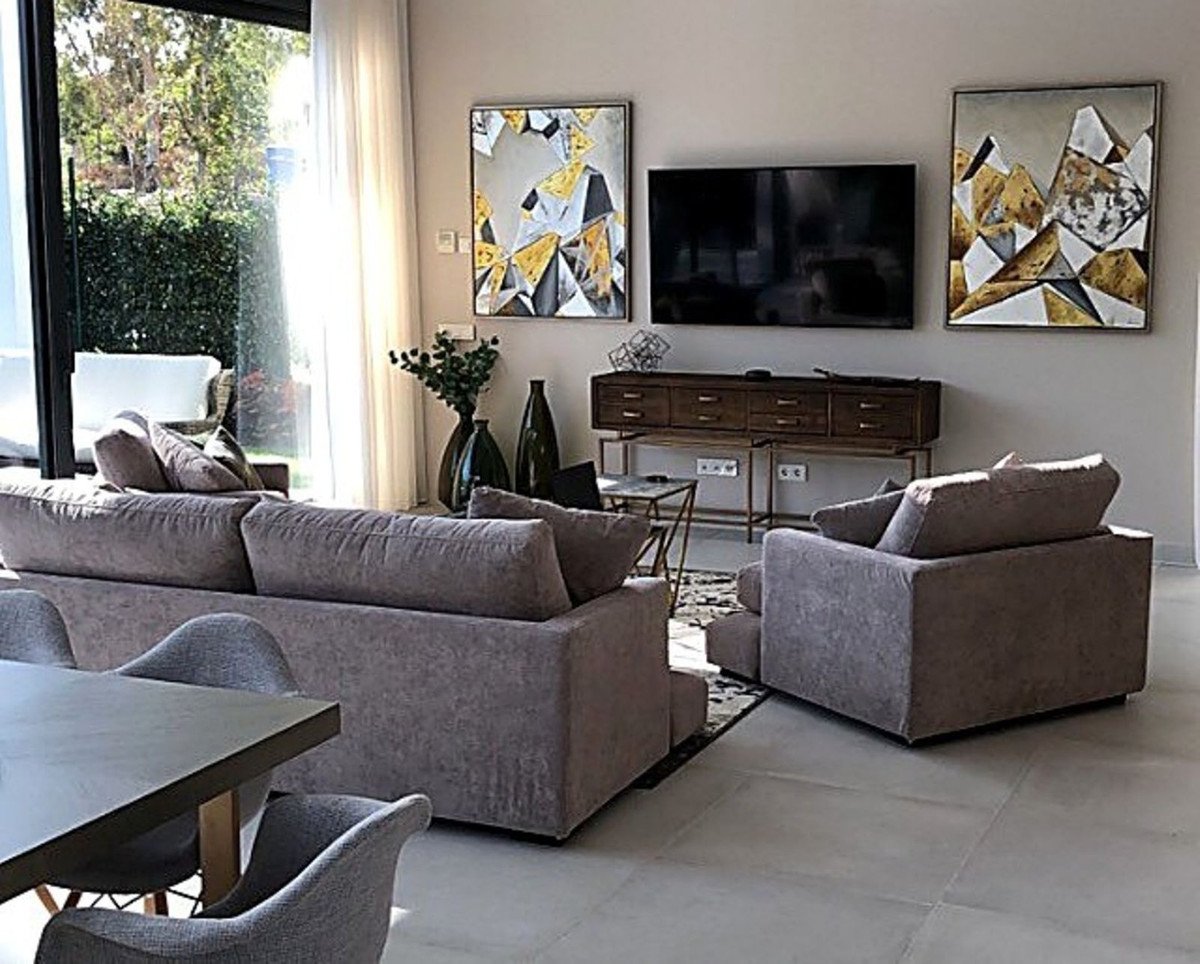 Modern living room with plush sofas, contemporary art, a large TV, and garden views through glass doors.