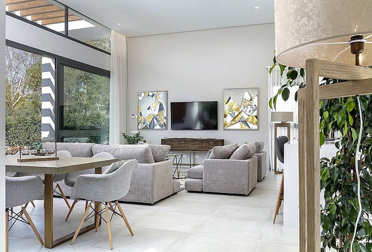 Modern living room with comfortable grey sofas, dining area, large windows with a garden view, and abstract art on the wall.
