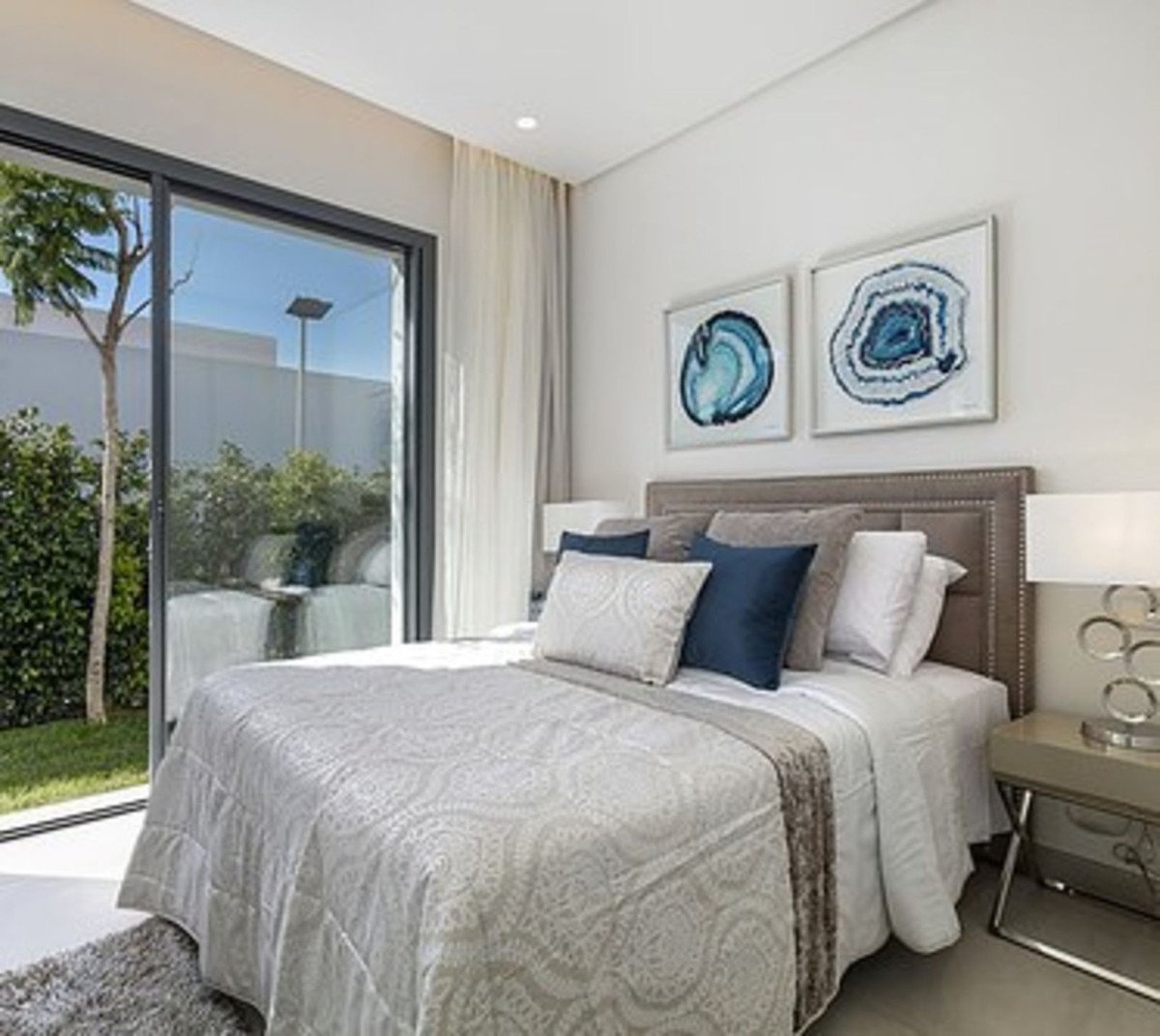 Modern bedroom with king-size bed, elegant bedding, and large glass doors opening to a lush garden.