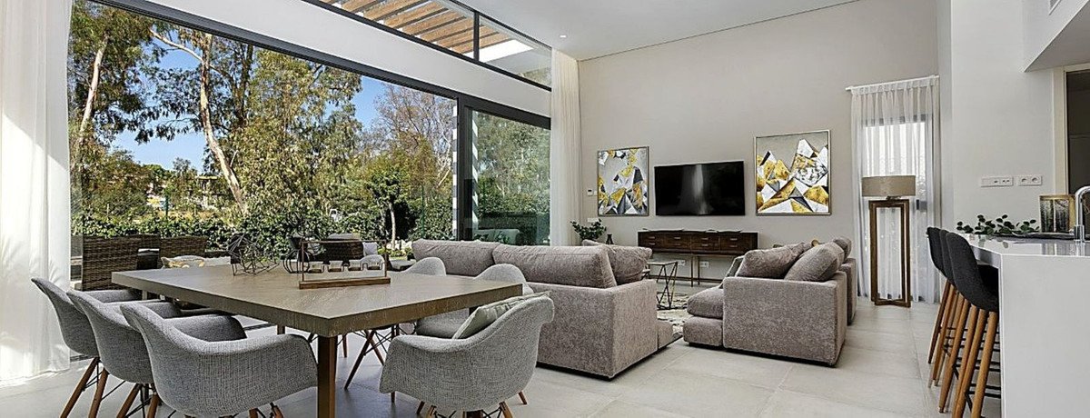 Modern living and dining area with large windows overlooking a lush garden and trees.