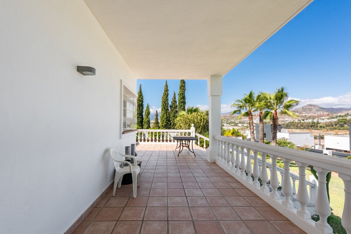 A spacious balcony with tiled flooring, outdoor seating, and a view of palm trees and distant mountains.