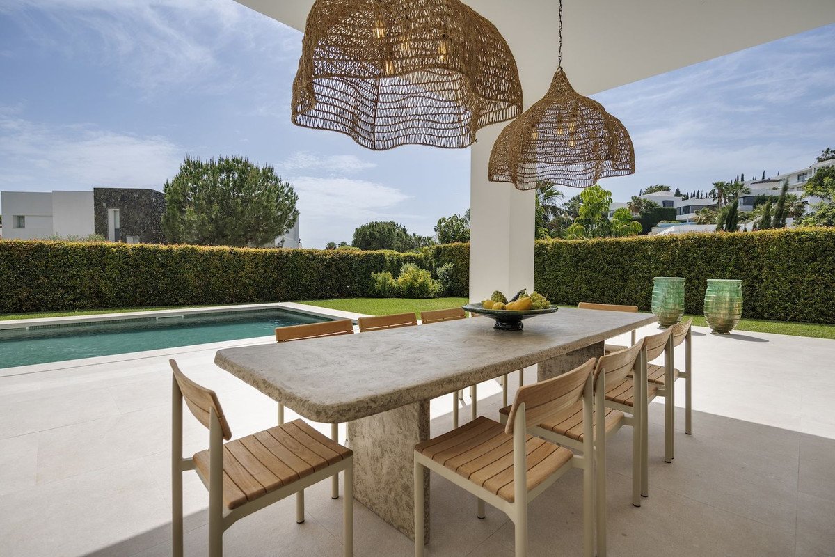 Outdoor dining area with pool view, wicker lamps, and modern furniture