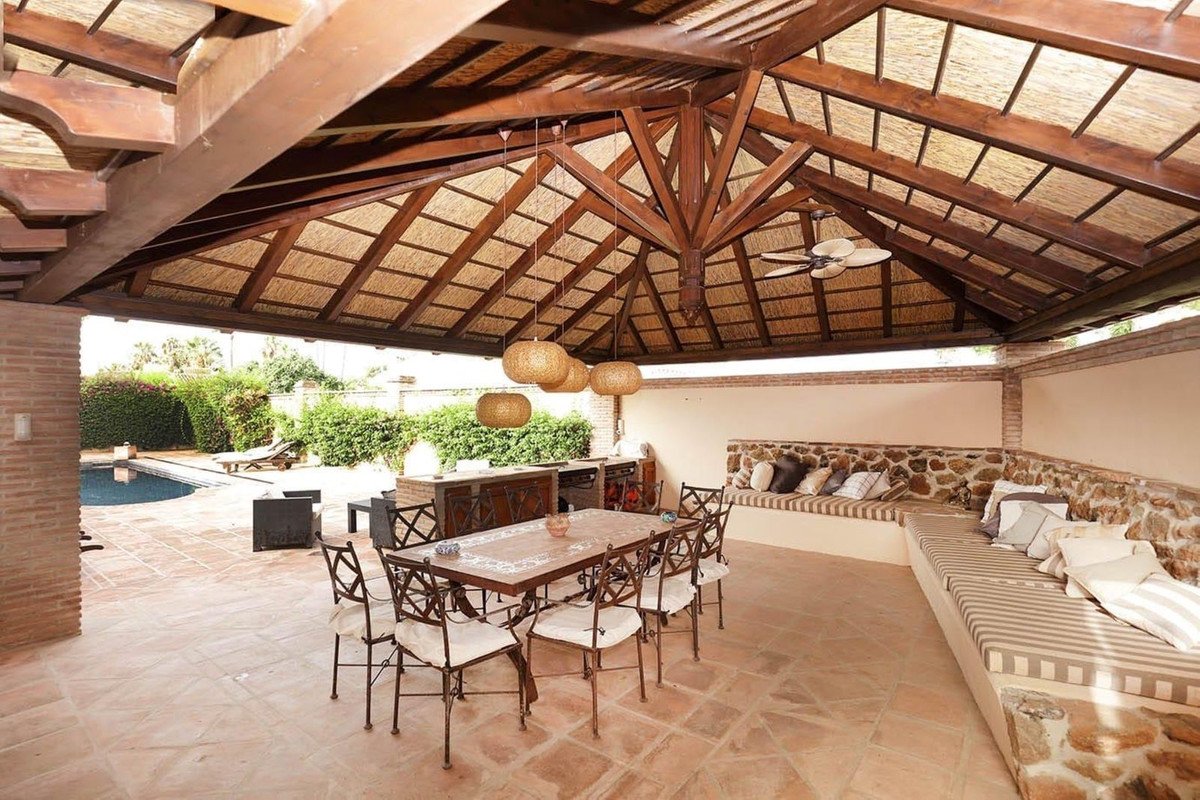 Covered patio with dining table, outdoor seating, and a view of the pool and garden.