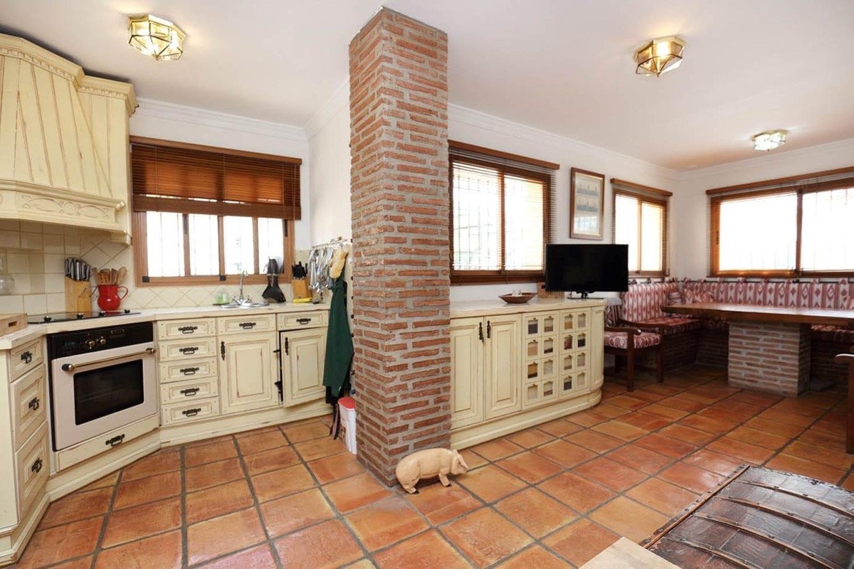Spacious kitchen and dining area featuring cream cabinetry, a brick pillar, a built-in bench seating, and terracotta tiled floors.