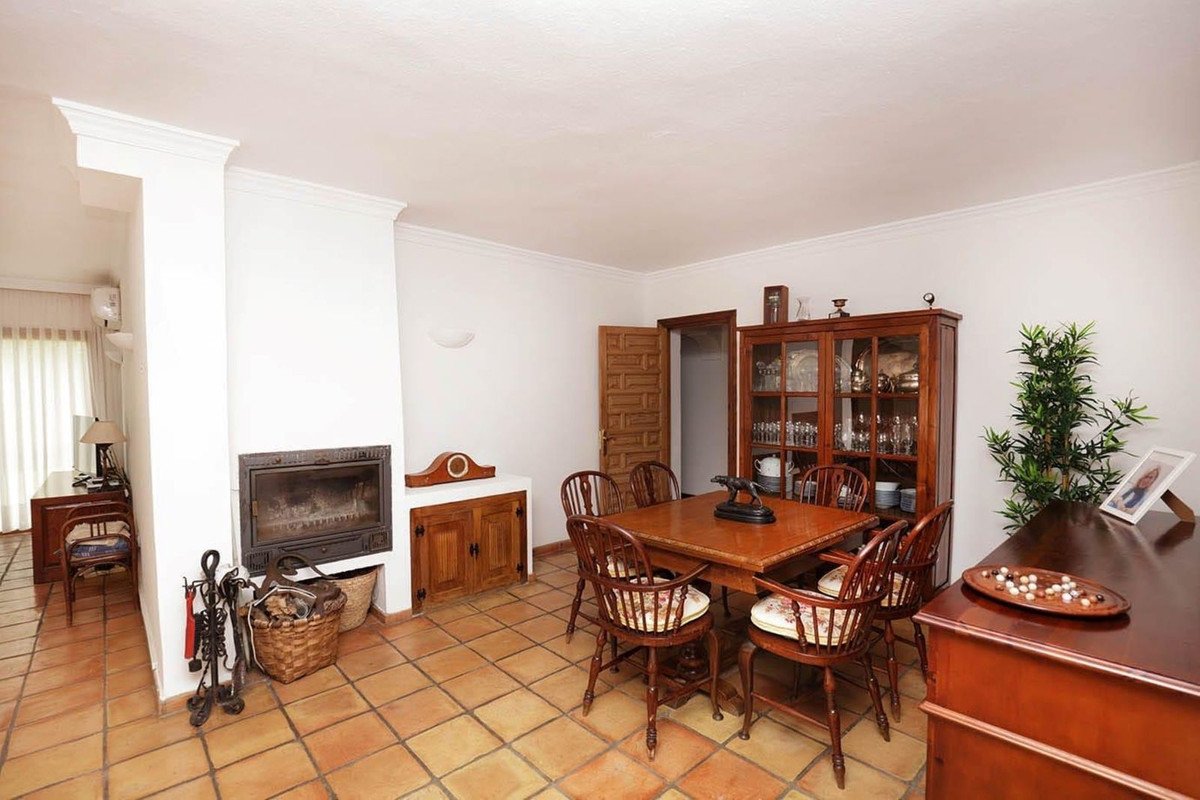 A dining room with a wooden table, chairs, fireplace, and a glass-fronted cabinet.