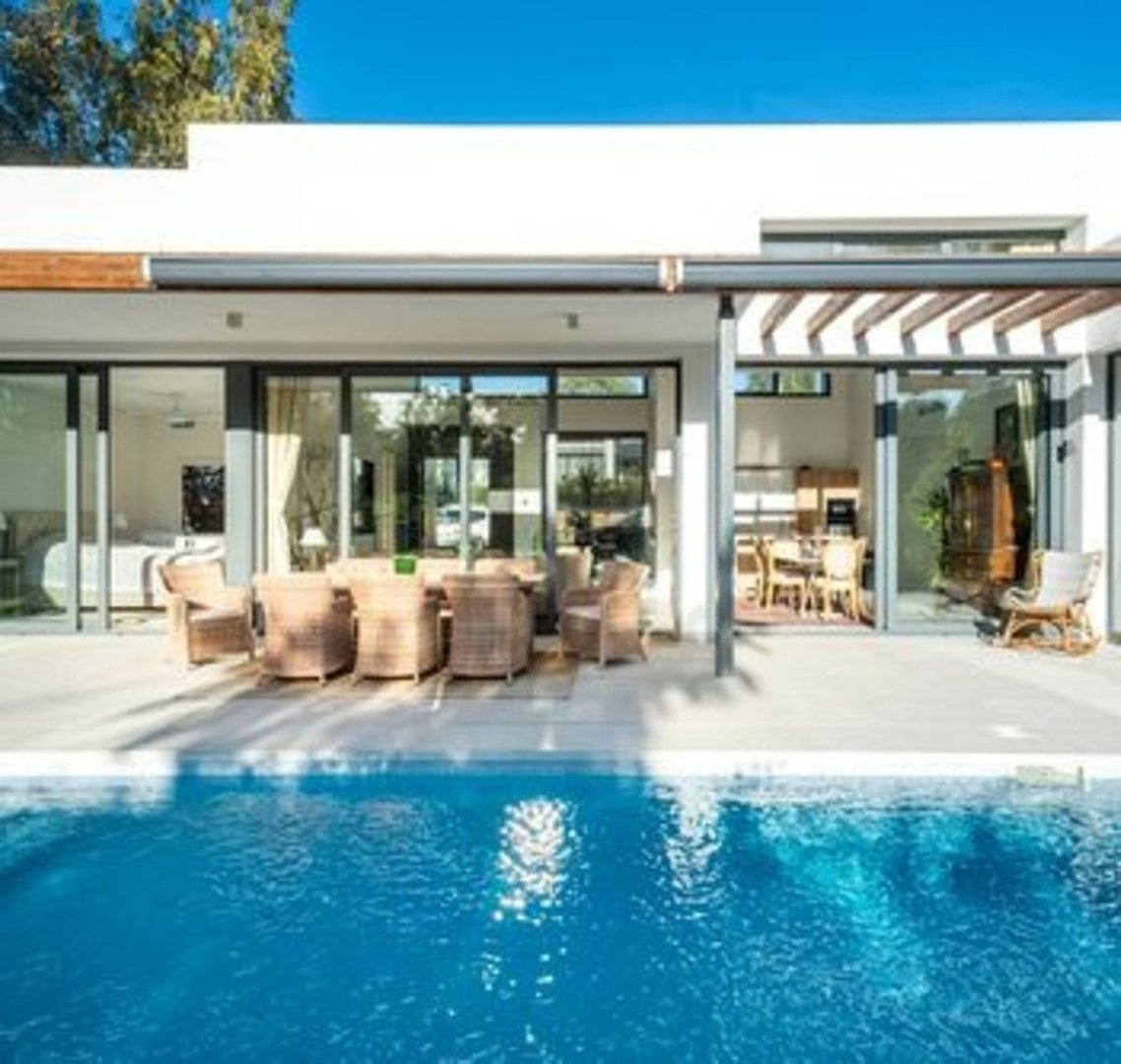 Modern villa with a swimming pool, outdoor dining set, and lounge furniture visible through glass doors.