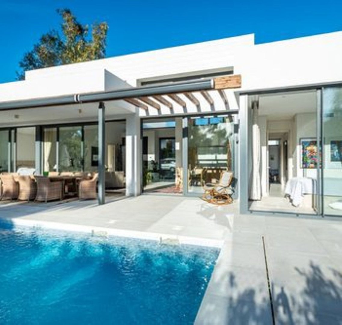 Modern house exterior with a swimming pool, outdoor dining area, and large glass sliding doors leading inside.