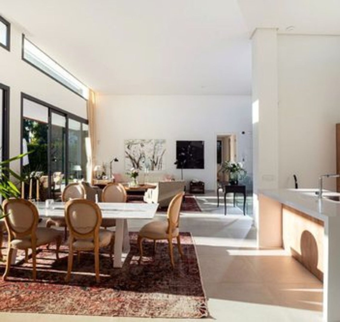 Spacious open-plan living and dining area with modern furniture, large windows, and a view of the kitchen.