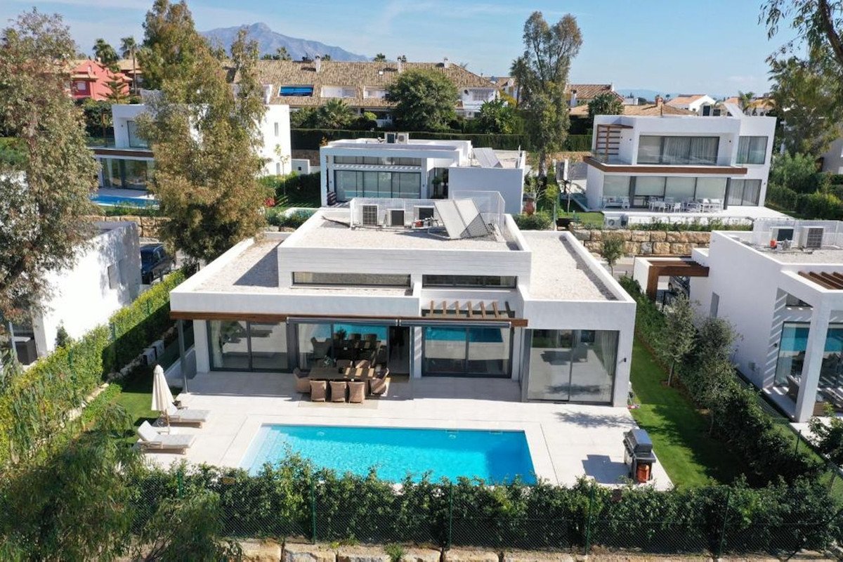 Modern villa with a swimming pool, outdoor dining area, and lounge chairs, set against a backdrop of hills.