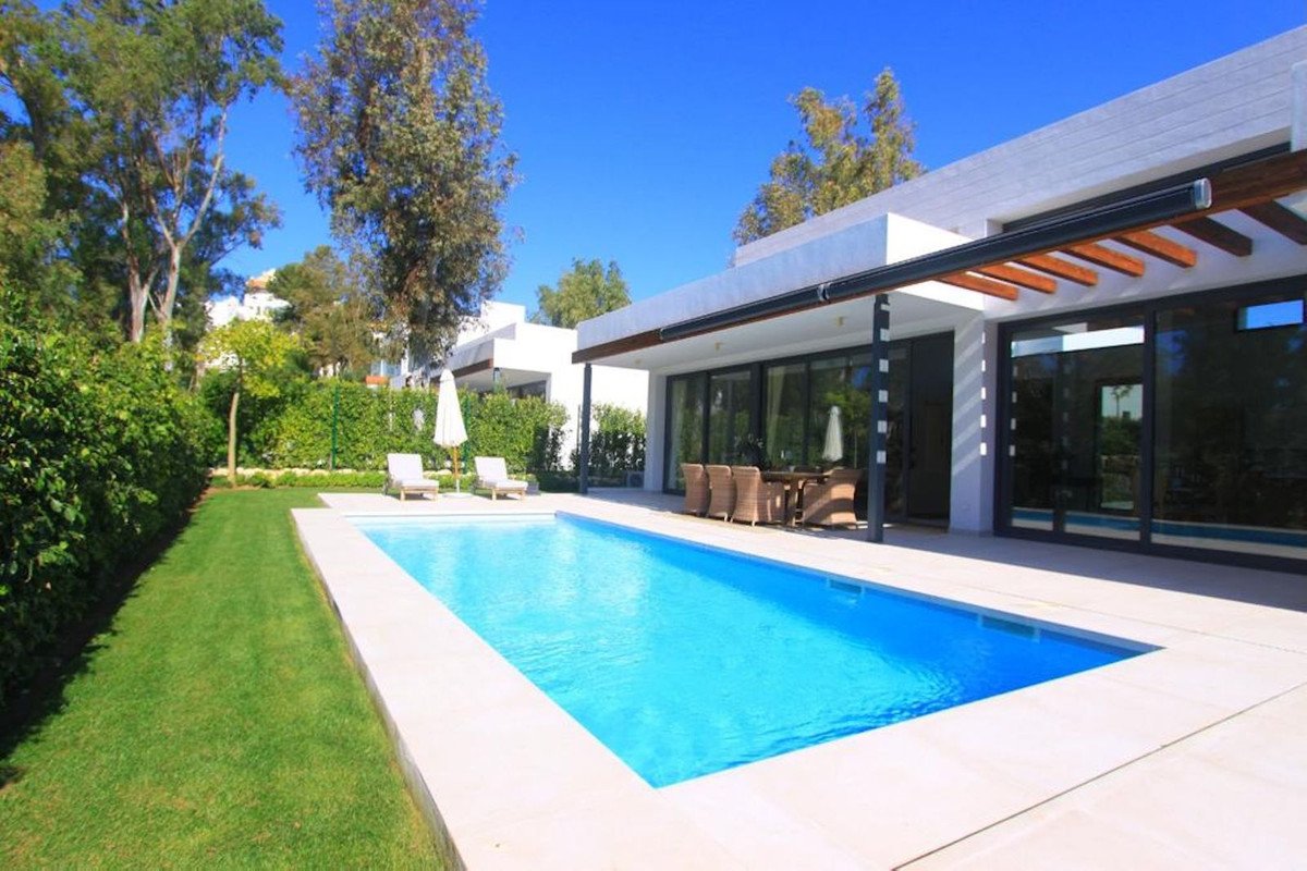 Modern villa with a rectangular swimming pool, lounge chairs, and an outdoor dining area under a pergola.