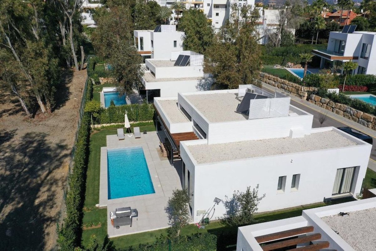 Modern white villa with a large swimming pool, sun loungers, and solar panels on the roof.