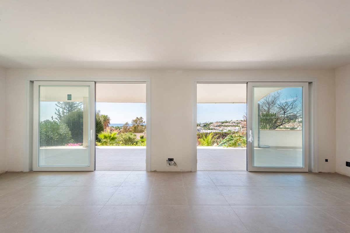Empty living room with large sliding doors opening to sea and landscape views