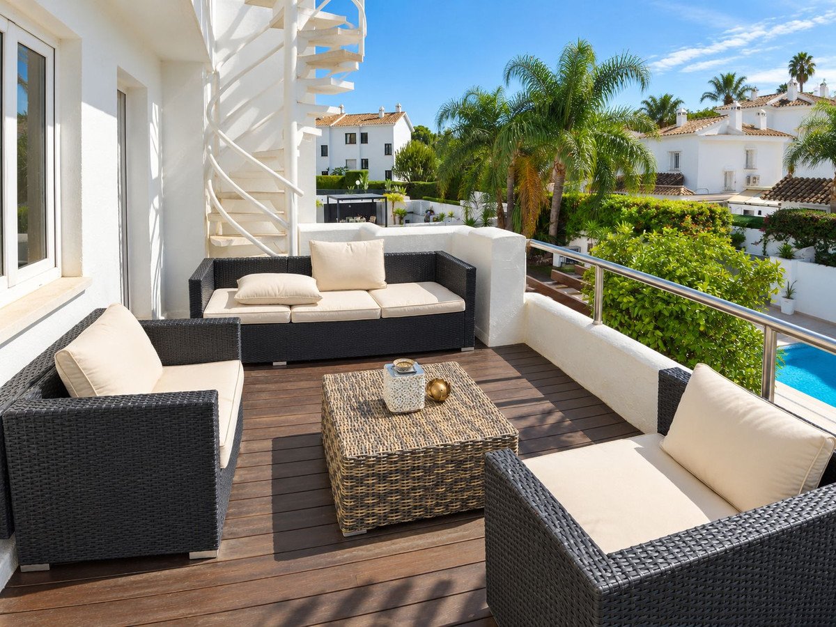 Modern balcony with outdoor seating, pool view, and palm trees.