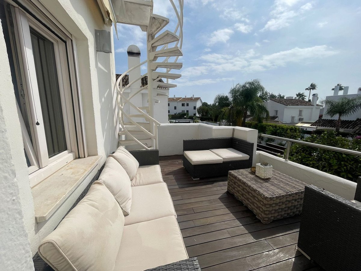 Outdoor terrace with spiral staircase, seating, and wooden flooring overlooking buildings