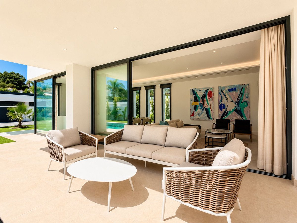 Modern patio with wicker and upholstered furniture, a white coffee table, and sliding glass doors opening to a living room.
