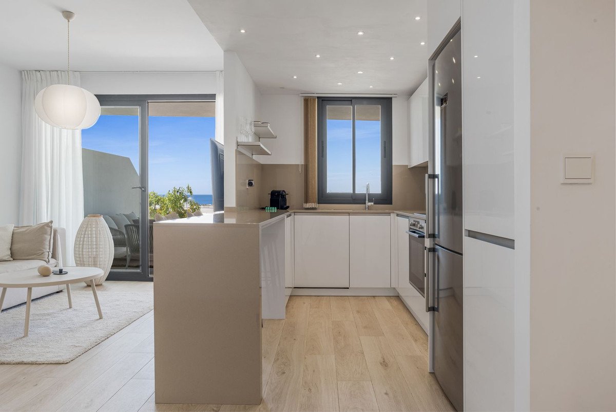 Modern living room and kitchen area with a balcony overlooking the sea. Features a sofa, coffee table, and a sleek kitchen.