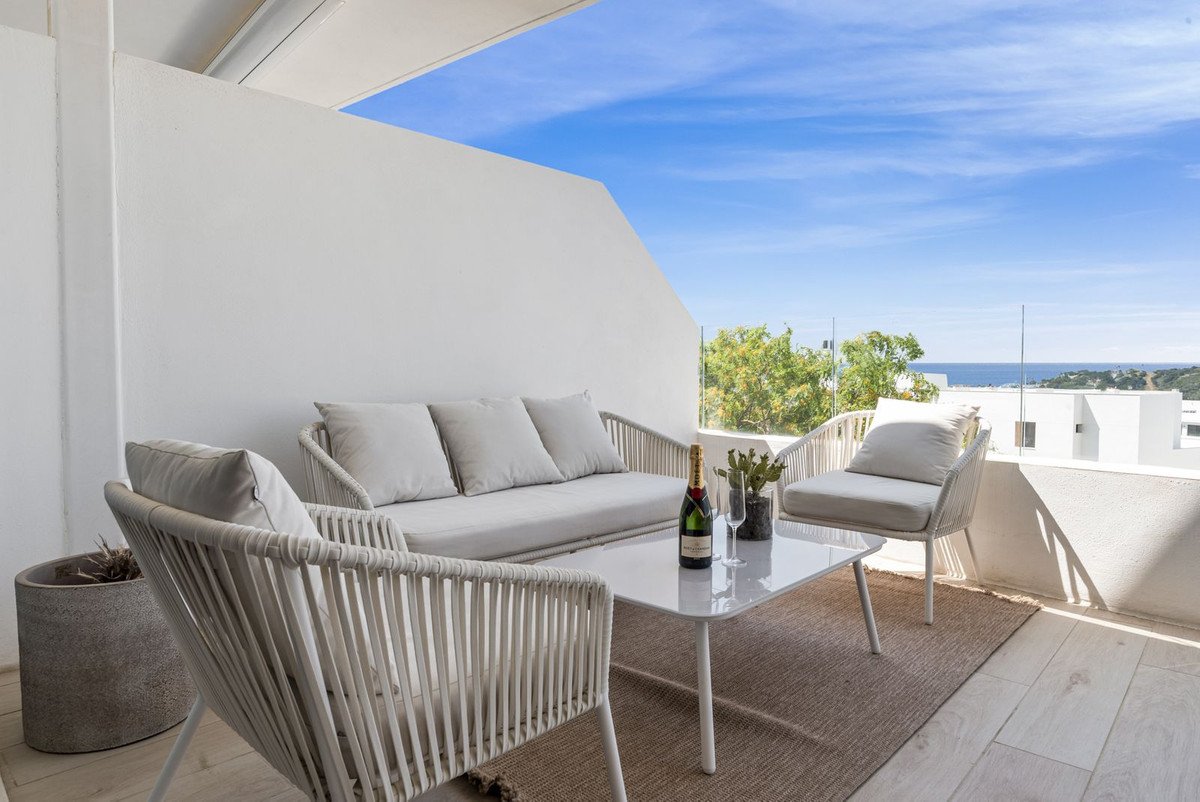 Outdoor terrace seating area with sofa, chairs, coffee table, champagne, and a view of the sea and sky.