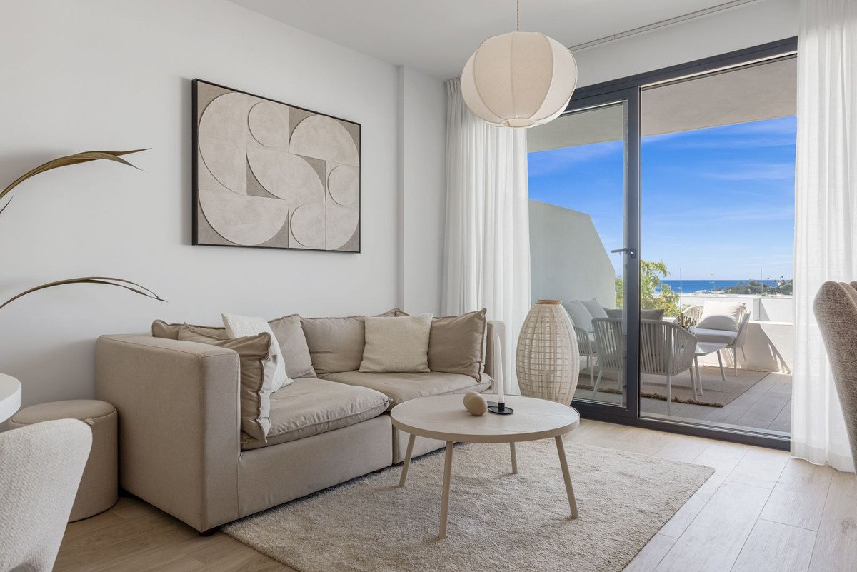 Modern living room with a sectional sofa, coffee table, and large sliding doors opening to a balcony with a sea view.