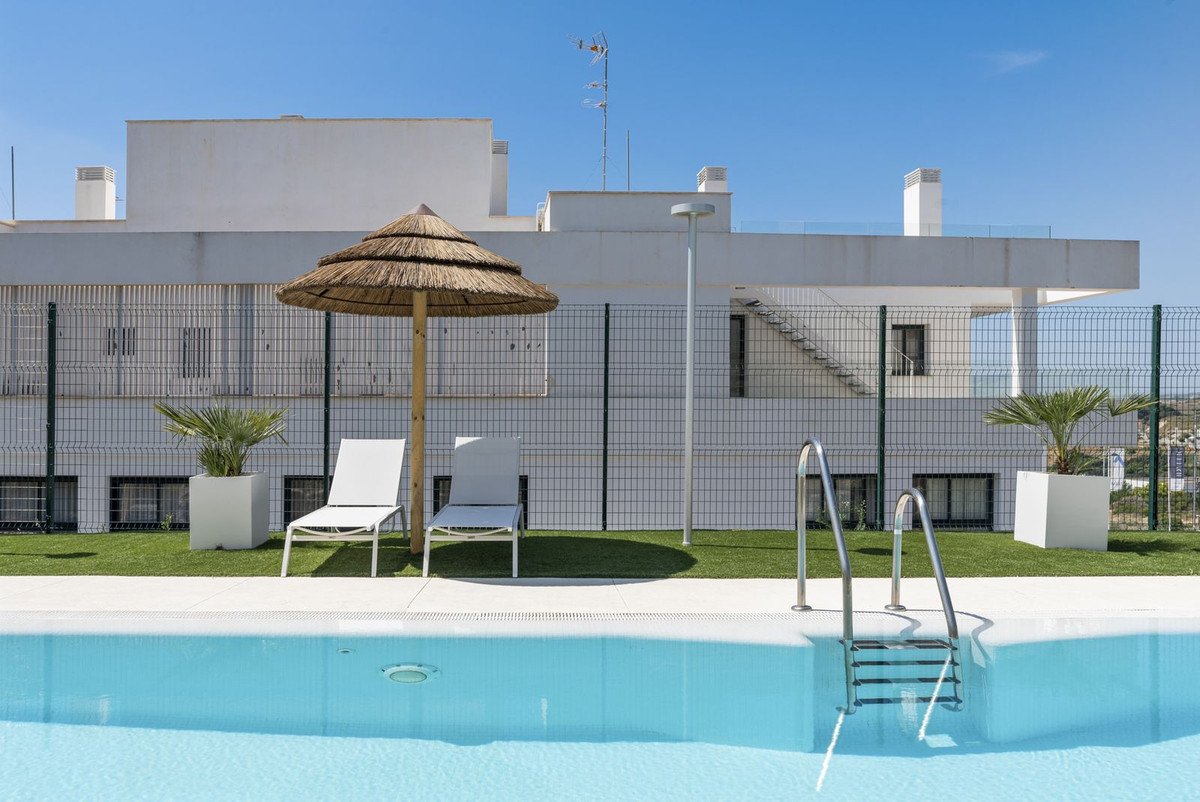 A bright swimming pool area with lounge chairs, a thatched umbrella, and modern building in the background.
