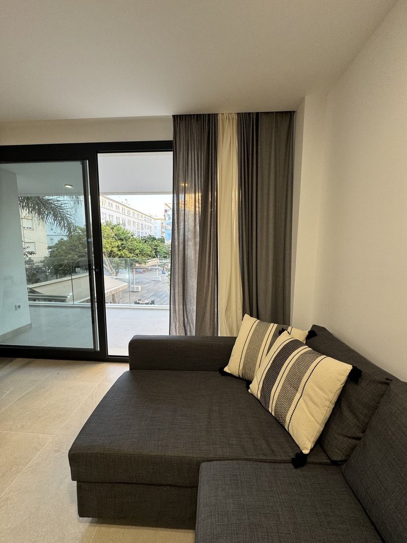 A dark grey sectional sofa with striped pillows sits in front of large sliding glass doors opening to a balcony and city view.