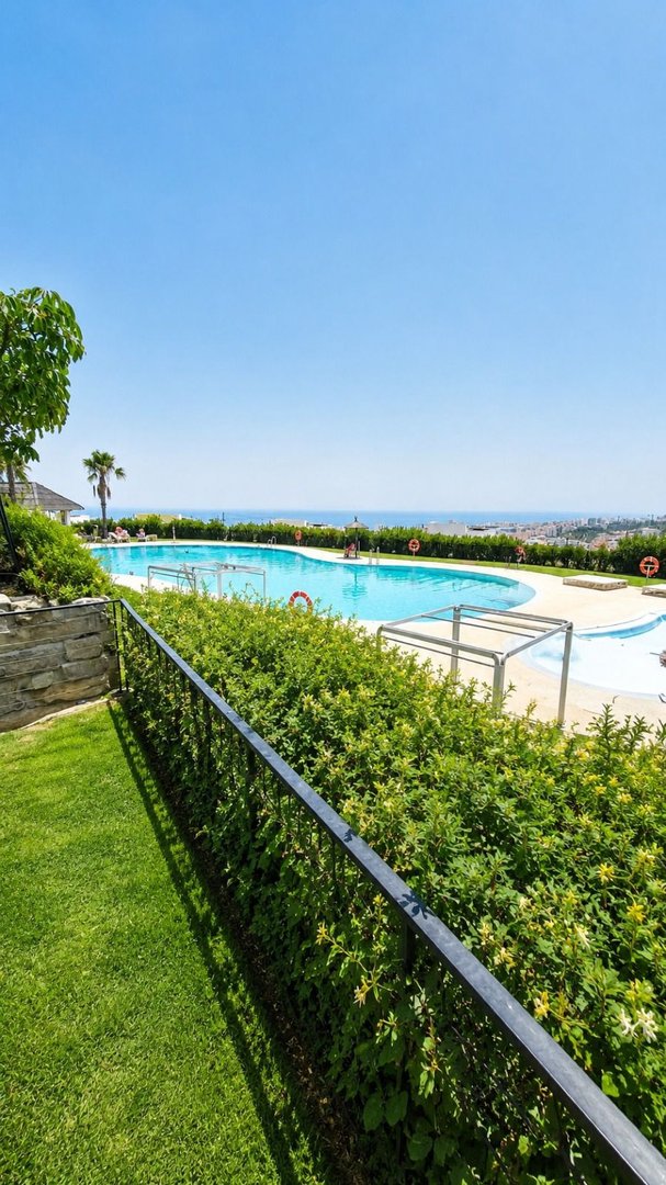 Communal swimming pool with sun loungers and a beautiful sea view on a sunny day.