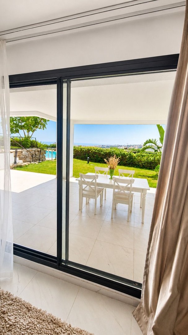 Terrace dining area with white table and chairs overlooking the sea and a swimming pool.