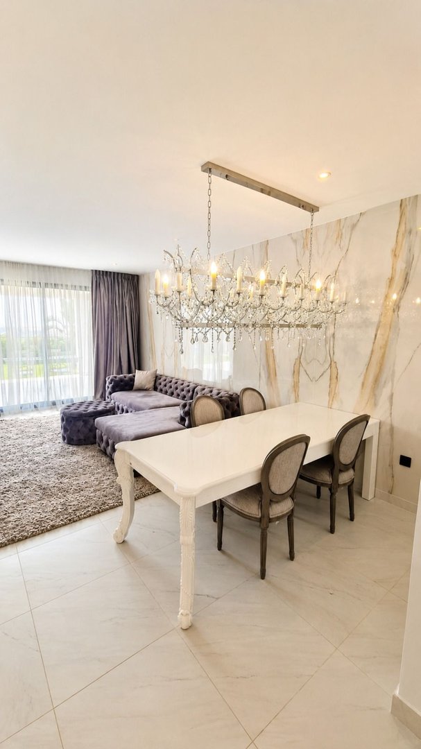 Luxurious living and dining area featuring a tufted sectional sofa, elegant chandelier, and marble accent wall.