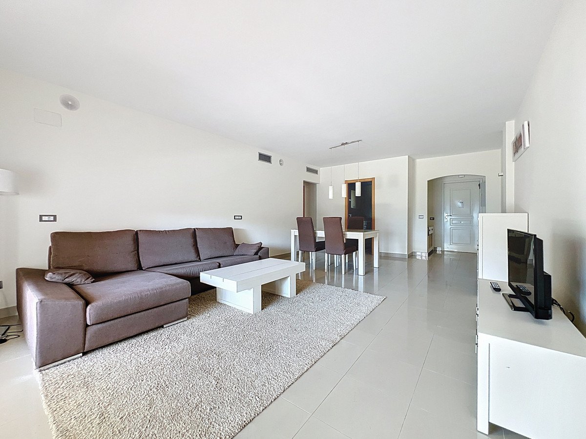 Modern living room with brown sofa, white coffee table, and dining area in open-plan space.