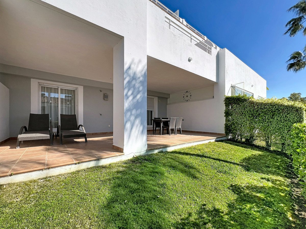 Modern white villa with covered patio, lounge chairs, dining table, and green lawn under blue sky.