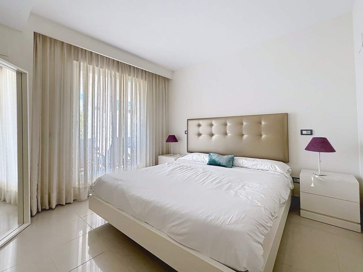 Modern bedroom with white bed, tufted headboard, and large window with sheer curtains.