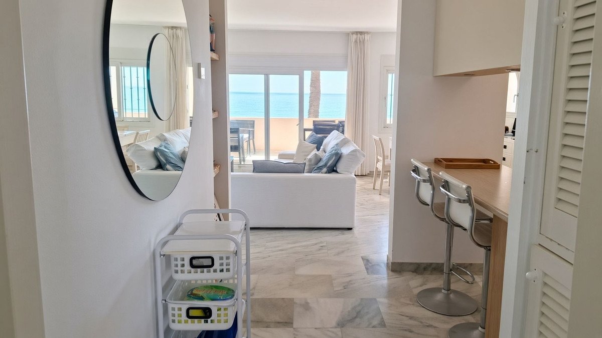 A bright living room with a white sofa and sea view through large glass doors. Includes a breakfast bar with stools.