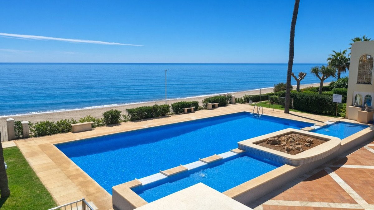 A bright blue swimming pool with a sea view, featuring beach access and palm trees on a sunny day.