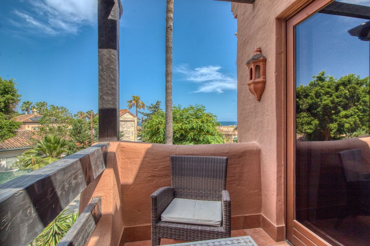 Balcony with wicker chair, ocean view, palm trees, and terracotta walls under blue sky.