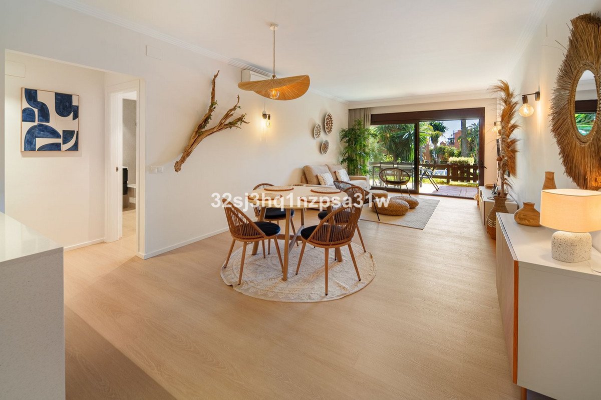 Modern living and dining area with natural wood furniture, a large window overlooking a lush garden and patio.