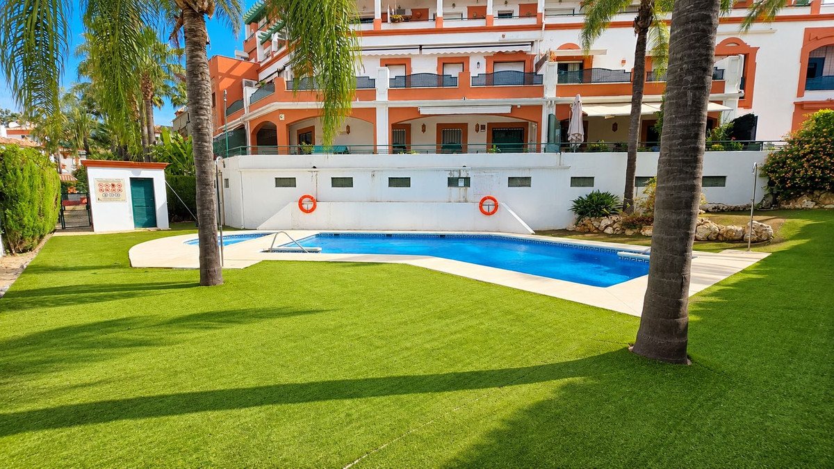 Villa with pool, palm trees, and lush green lawn, featuring a multi-story building with orange and white facade.