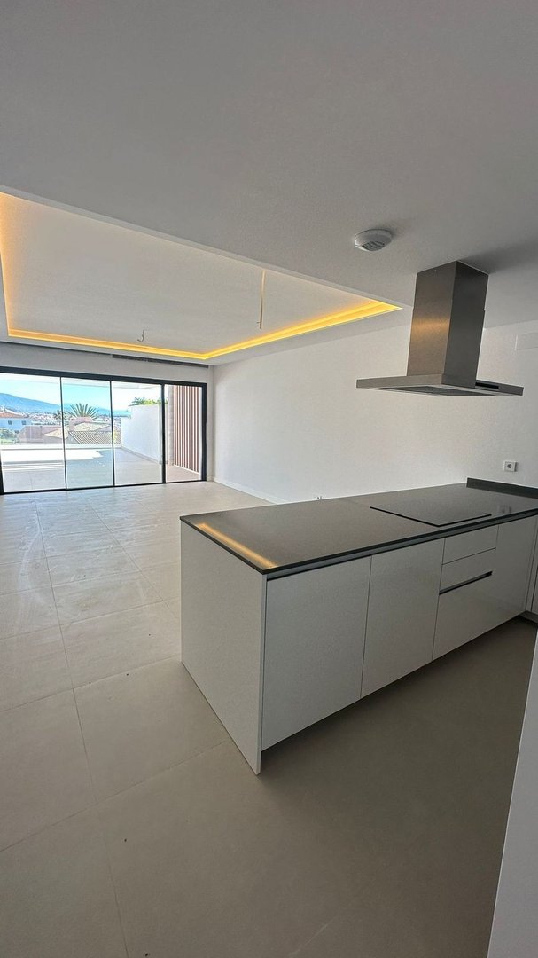 Modern open-plan living area with kitchen island, large windows, and a balcony with a sea view.